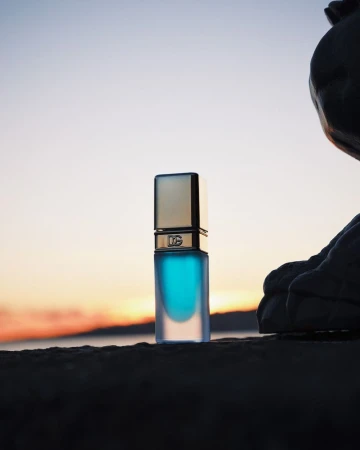 Dolce & Gabbana perfume bottle on a rock with a sunset backdrop, reflecting luxury and sophistication in a natural setting.