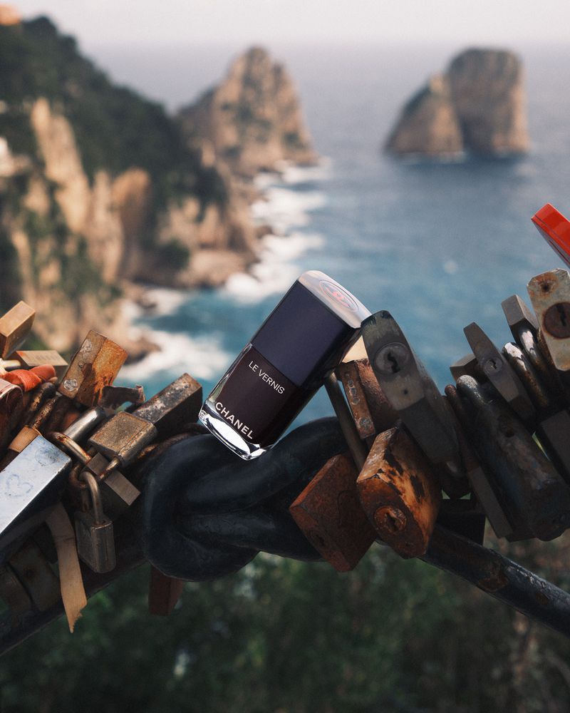 Nail polish by Chanel on a metal structure with locks, blurred sea and rock formations in the background, beauty and travel concept.
