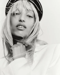 Close-up monochrome portrait of Mona Tougaard wearing a dark headband and light blazer against a white studio background.