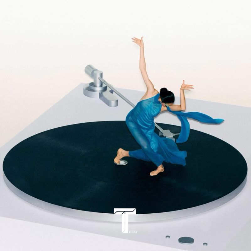 A dancer in a blue dress poses elegantly on a black turntable platform against a clean white background in a stylized fashion shot.