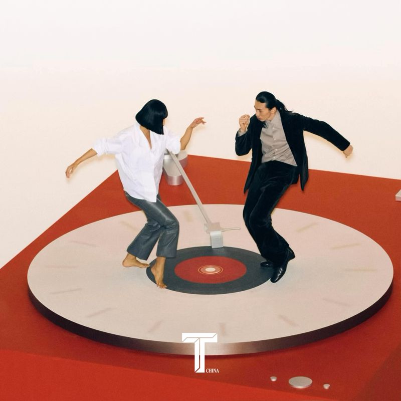 Two people in fashionable attire dance on an oversized red-and-white vinyl record, set against a stark white backdrop.