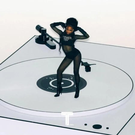 Woman in mesh bodysuit and heels stands on a white turntable against a white background in a fashion or music editorial.