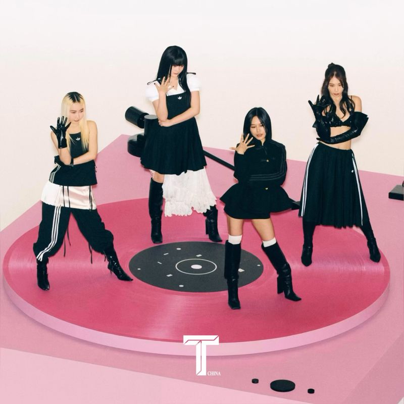 Four women in dark outfits pose on a pink turntable in a studio setting, presenting a stylish and musical-themed image.