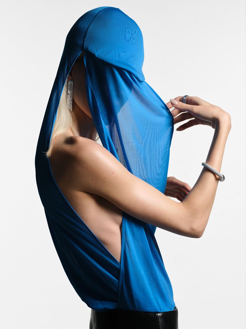 Model wearing a bright blue head covering and dress with jewelry in a studio setting, creating a striking fashion image. 