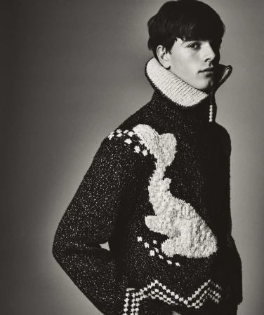 Monochromatic portrait of a young man wearing a patterned wool sweater with a high collar, eyes forward, in a studio setting.