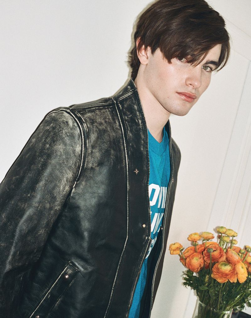 Young man wearing a dark leather jacket over a blue t-shirt with a vase of orange flowers in the foreground