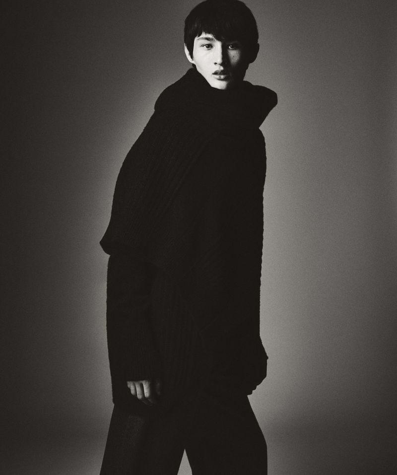 Young man in dark high-neck winter sweater standing against a gradient studio backdrop for HERO Magazine.