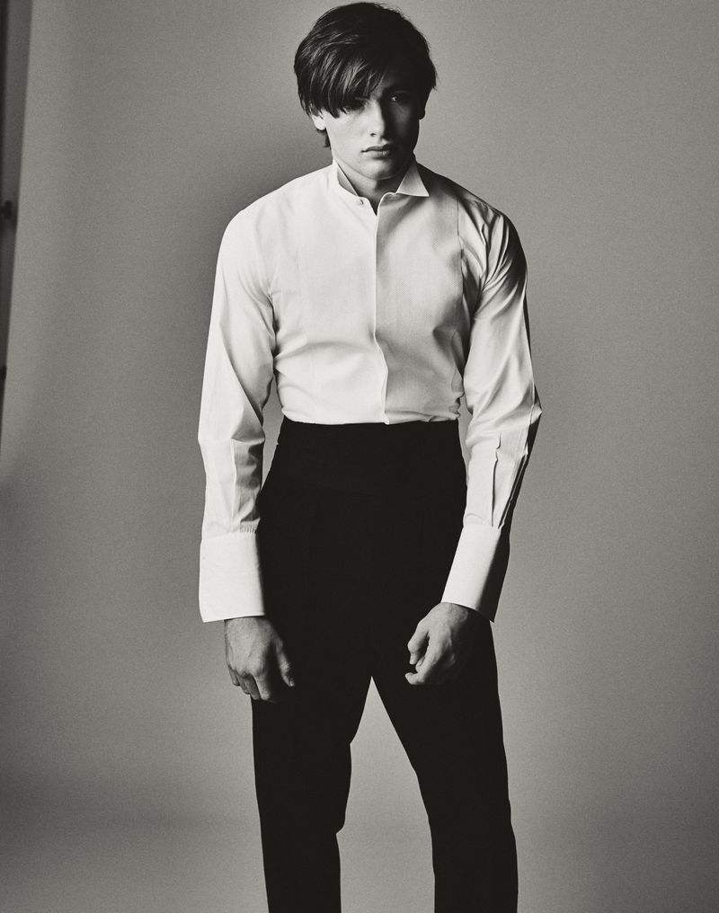 Monochrome portrait of a young adult male wearing a white dress shirt and black pants in a photo studio with neutral lighting.