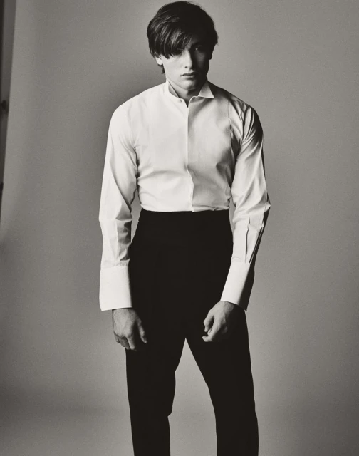 Monochrome portrait of a young adult male wearing a white dress shirt and black pants in a photo studio with neutral lighting.