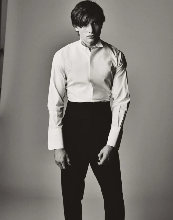 Monochrome portrait of a young adult male wearing a white dress shirt and black pants in a photo studio with neutral lighting.