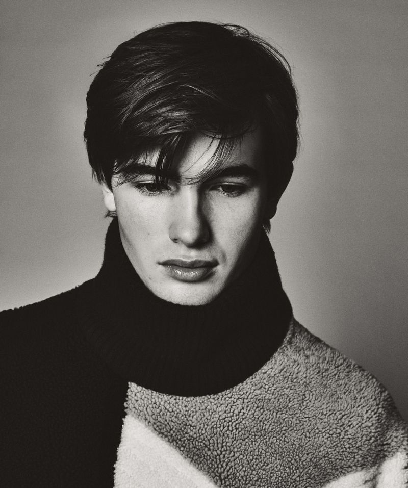 Monochrome portrait of a young adult male with dark hair and a neutral expression wearing a sweater against a plain background.