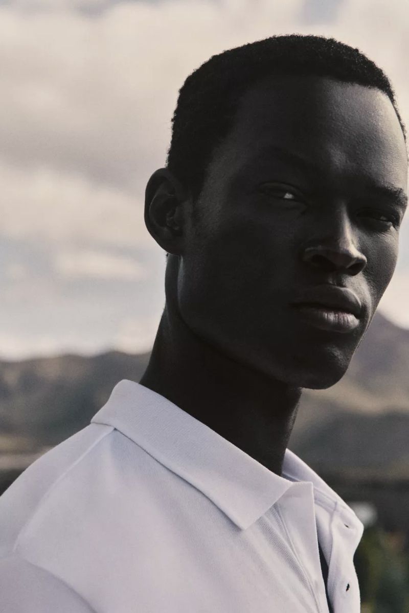 Portrait of an African American man in a white shirt against a mountain backdrop. The photo captures a clean and minimalist aesthetic.