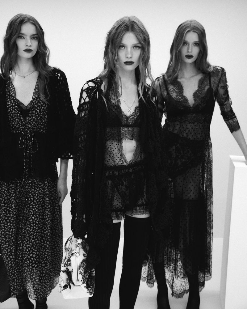 Three female models wearing black lace dresses and dark lipstick posing against a white studio background.