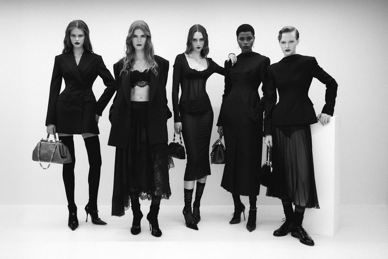 Five fashion models pose in black attire in a studio setting with a white background, displaying high-fashion, elegant designs and handbags.