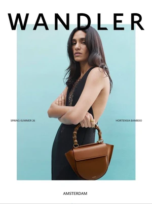 Woman in a black dress holding a brown leather handbag with a bamboo handle against a blue background