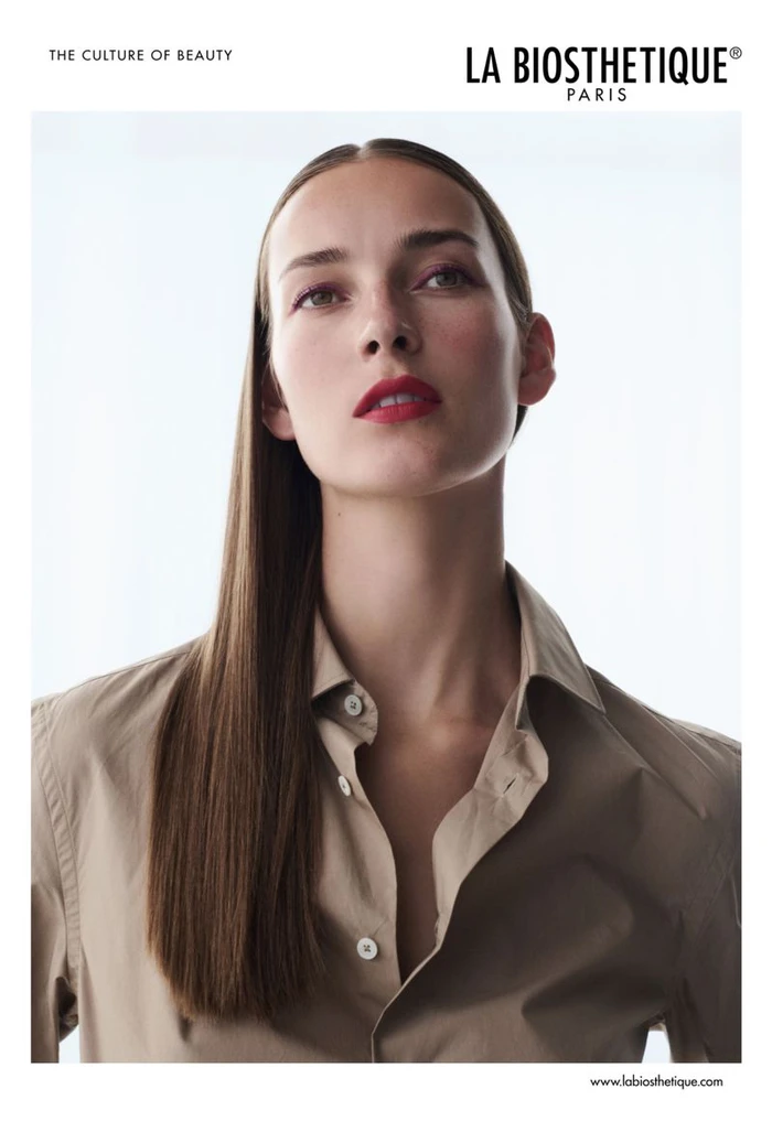 Model Julia Bergshoeff with sleek straight brown hair wearing a beige buttoned shirt against a bright white background.
