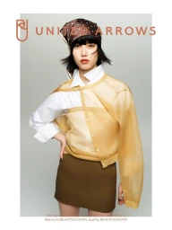 Model wearing a white shirt, sheer yellow top, brown skirt, and polka-dot headscarf against a grey backdrop.
