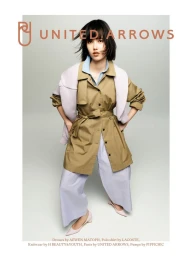 Model wearing khaki trench coat and light blue shirt against a neutral grey studio background with United Arrows branding