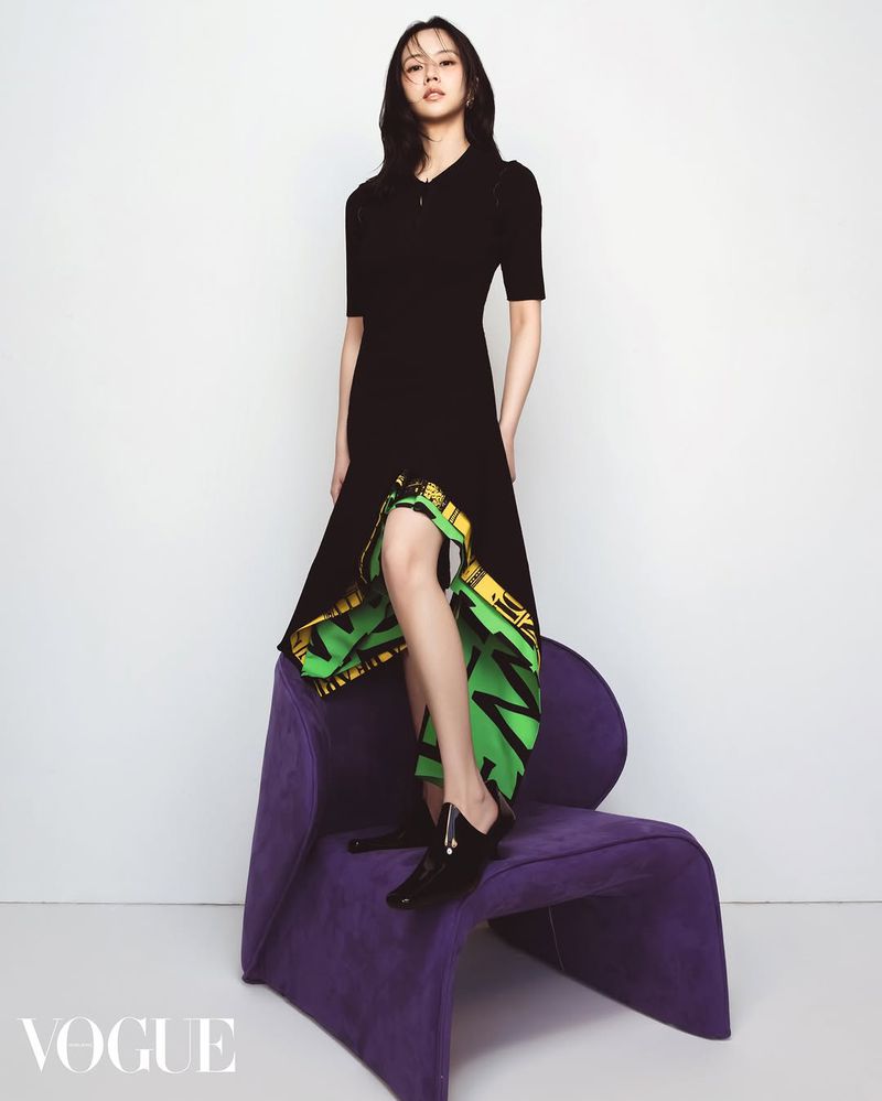 A fashionable young woman poses in a black dress on a purple chair against a white backdrop in a studio shot.