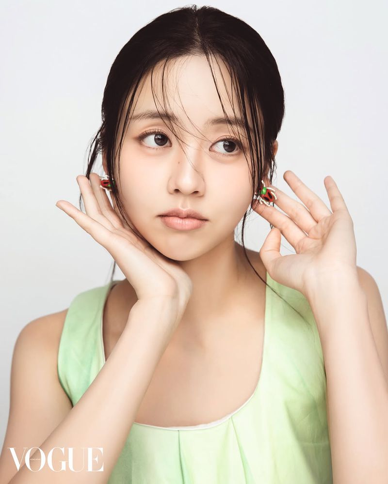 Close-up portrait of a young Asian woman with dark hair, wearing a pale green top and statement earrings against a white backdrop.