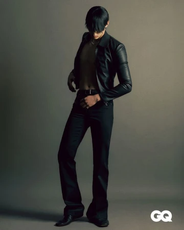 Fashionable man in leather jacket and flared pants poses in a studio, showcasing a blend of classic and contemporary style.
