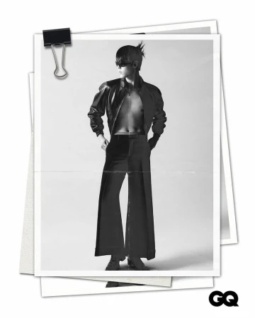 Black and white photograph on paper of a person with spiky hair wearing a leather jacket, dress pants, and heeled shoes against light backdrop.