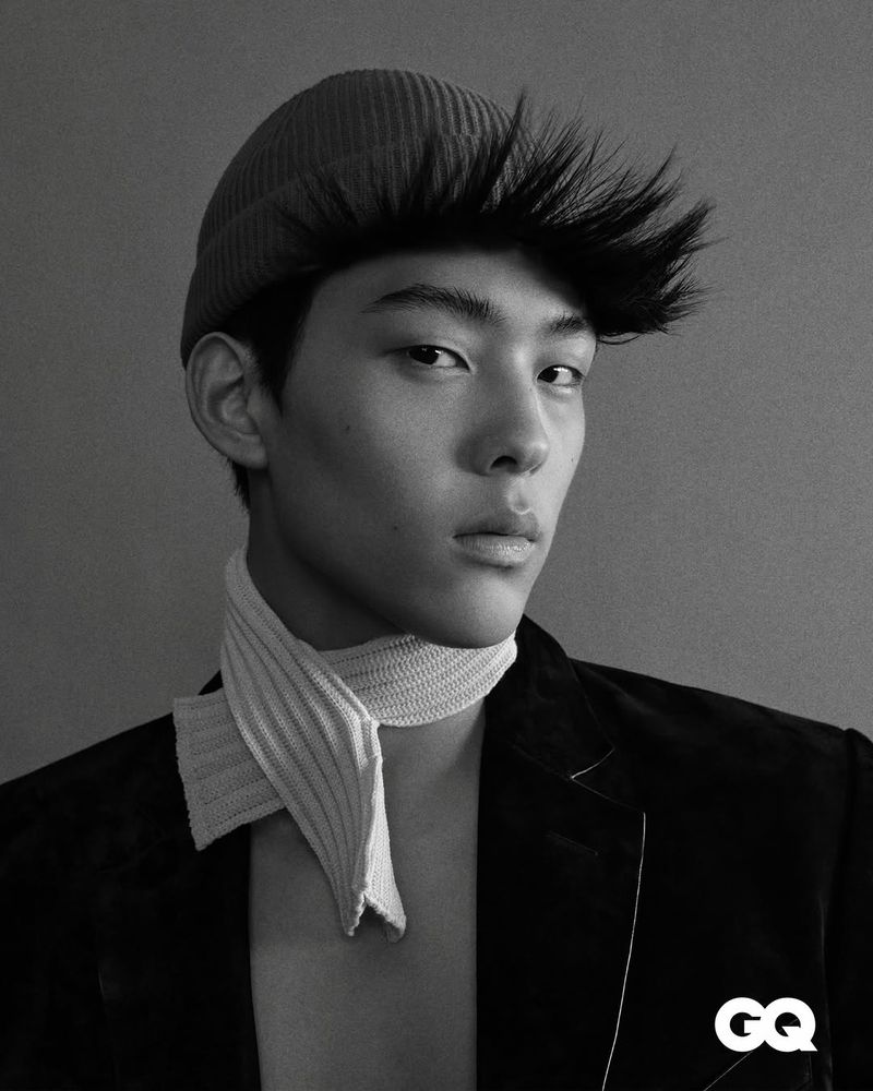 Monochrome portrait of an Asian man wearing a beanie, jacket, and neck scarf, set against a grey background, with the GQ logo.
