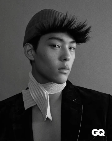 Monochrome portrait of an Asian man wearing a beanie, jacket, and neck scarf, set against a grey background, with the GQ logo.