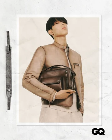 Handsome male fashion model poses in a neutral color leather jacket holding a dark brown leather briefcase in a studio fashion shot.