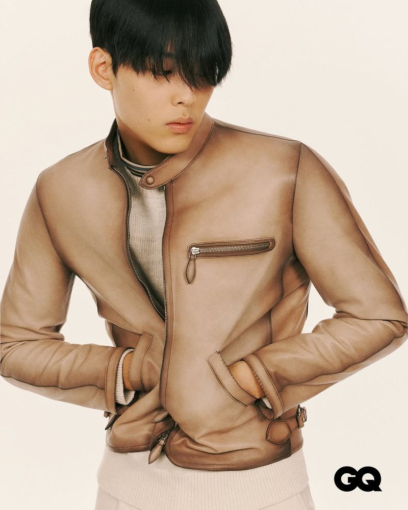 Portrait of a young adult wearing a leather jacket and casual attire against a neutral background, showcasing fashion and style.