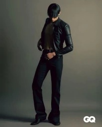 Man wearing a black leather jacket and black trousers posing against a grey studio backdrop for GQ Hong Kong.