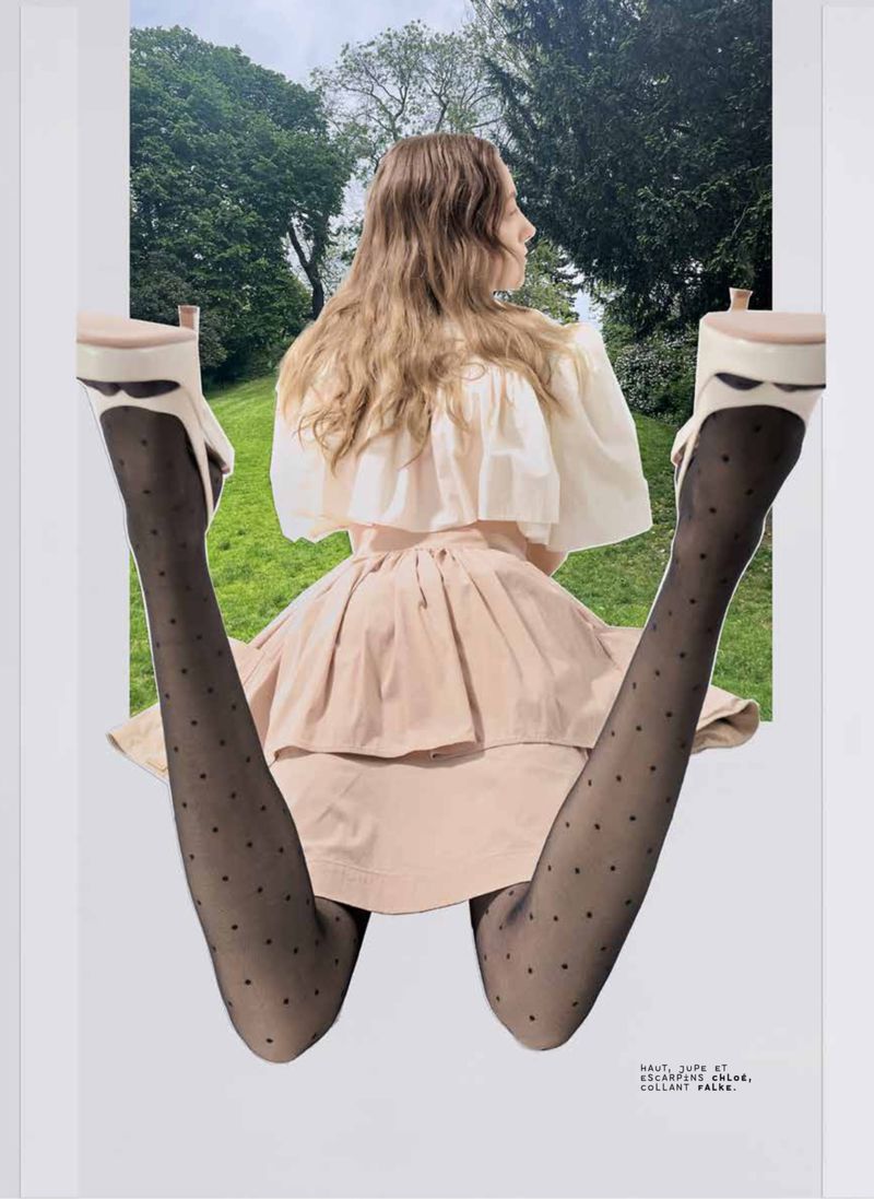 Woman in light pink dress with black polka dot tights and platform heels posing in front of a green outdoor landscape.