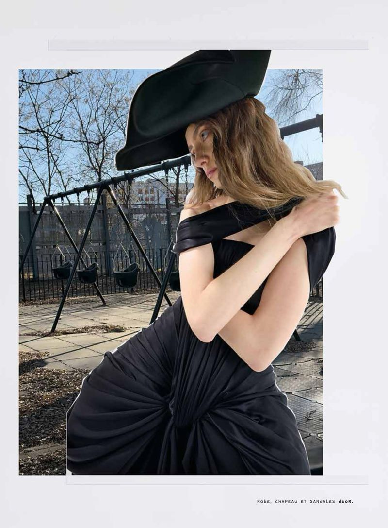 Fashion shot of a woman in a black dress and large hat, posed in front of a playground on a sunny day, with a white border.