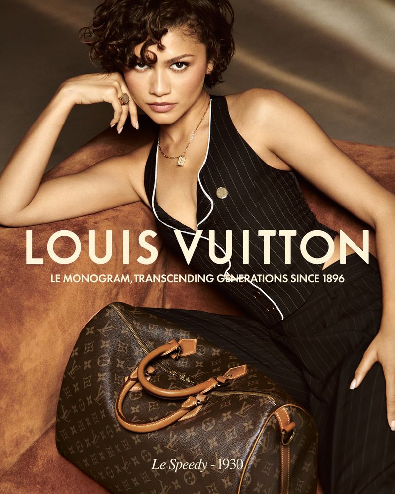 Zendaya poses with a Louis Vuitton handbag, modelling a black pinstripe vest and pants. Shot in a warm-toned studio.  