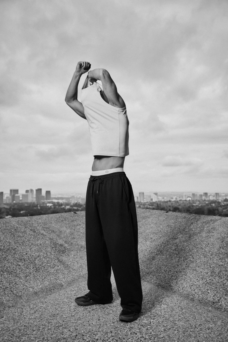 Black and white portrait of a muscular man in workout clothes standing on a gravel mound with a city skyline in the background.