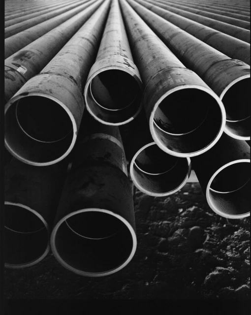 Monochrome image of stacked metal pipes creates an industrial pattern, emphasizing depth and texture in an urban environment.