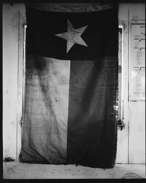 Distressed three-color flag with a large star hanging in a weathered doorway, creating a vintage and textural composition.
