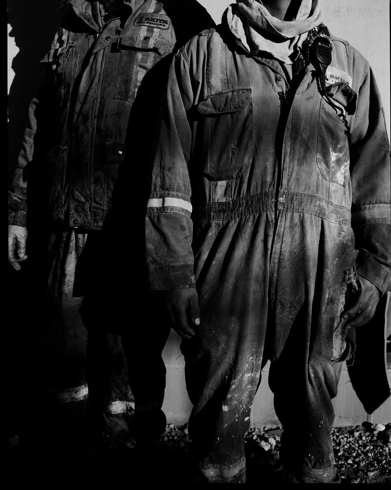 Two people stand in work coveralls, one in sharp focus, and the other person's shadow falls on a wall alongside them.