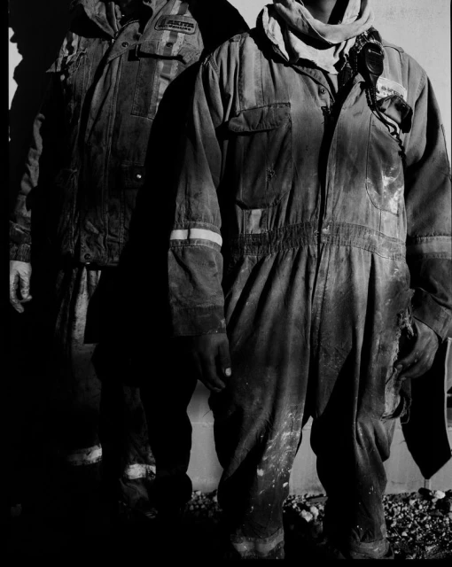 Two people stand in work coveralls, one in sharp focus, and the other person's shadow falls on a wall alongside them.