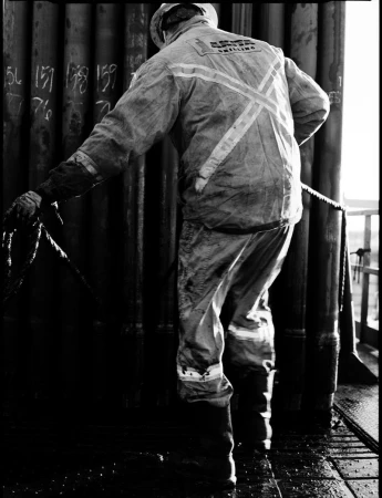 Monochrome shot of a worker in uniform gripping a rope near industrial pipes, highlighting labor and industry in a gritty, textured environment.