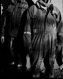 Monochrome portrait of two workers in heavy-duty utility overalls against a plain background