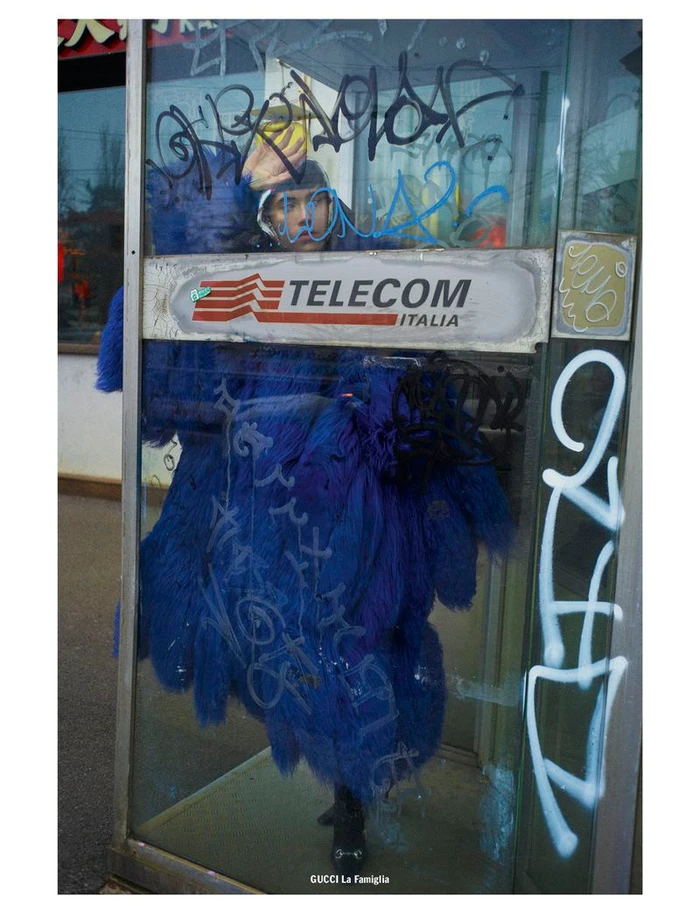 Model in blue feathered coat inside a graffiti-covered Telecom Italia telephone booth shot by Cedric Buchet for 10 Magazine