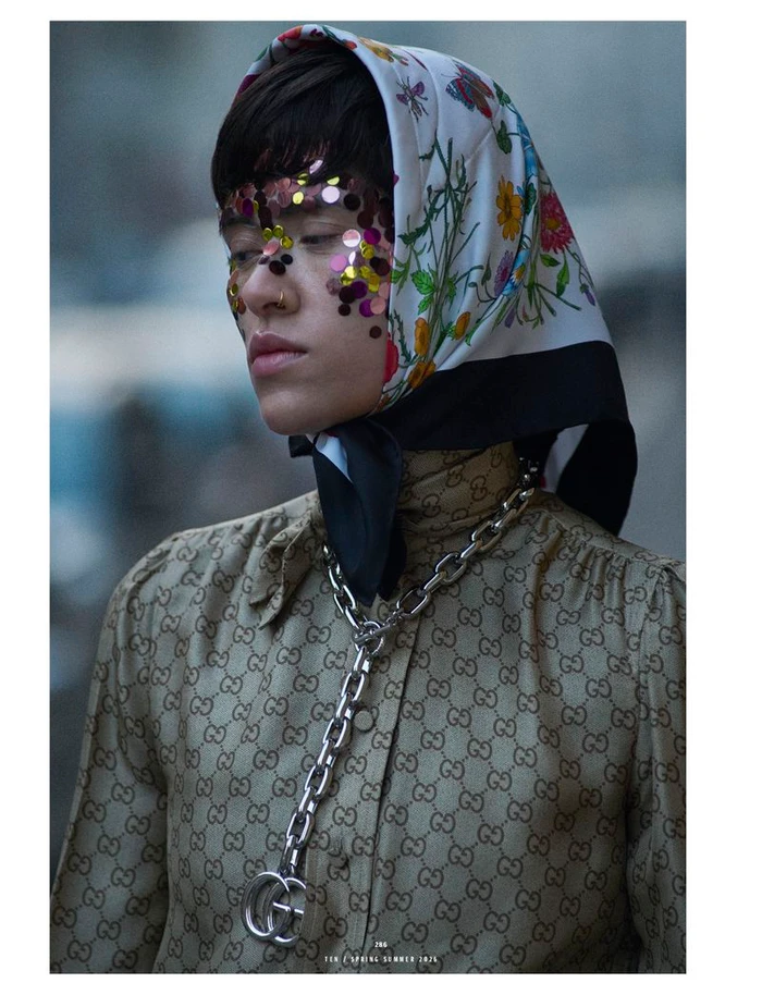 Model wearing a floral silk headscarf, monogrammed top, and heavy chain necklace with sequin facial embellishments