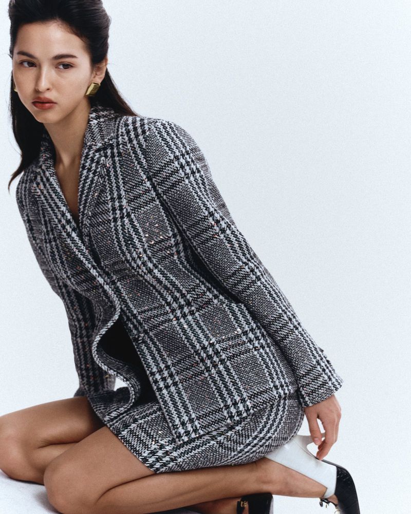 Woman kneeling in a grey plaid blazer and skirt set against a seamless white studio background