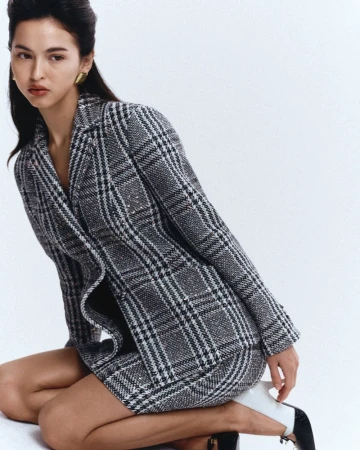 Woman kneeling in a grey plaid blazer and skirt set against a seamless white studio background