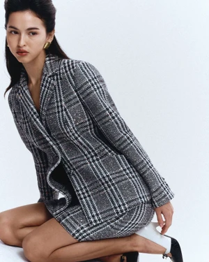Woman kneeling in a grey plaid blazer and skirt set against a seamless white studio background