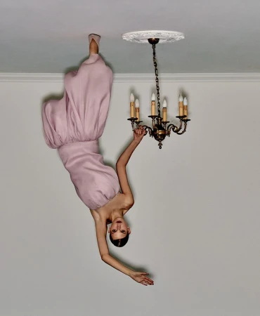 Model in pink dress touching an inverted chandelier on a ceiling, creating an upside-down illusion for Telegraph Luxury