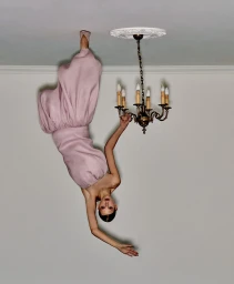 Model in pink dress touching an inverted chandelier on a ceiling, creating an upside-down illusion for Telegraph Luxury