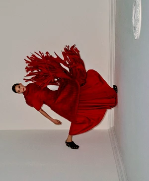 Model in a voluminous red fringed dress posing against a pale wall for Telegraph Luxury
