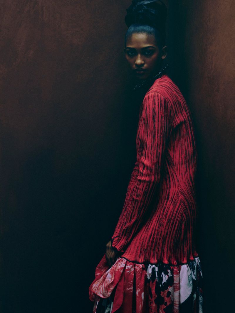 Fashion shot of a Black female model in a red textured dress with a floral skirt in a dark photo studio. Fashion, clothing, and portrait.
